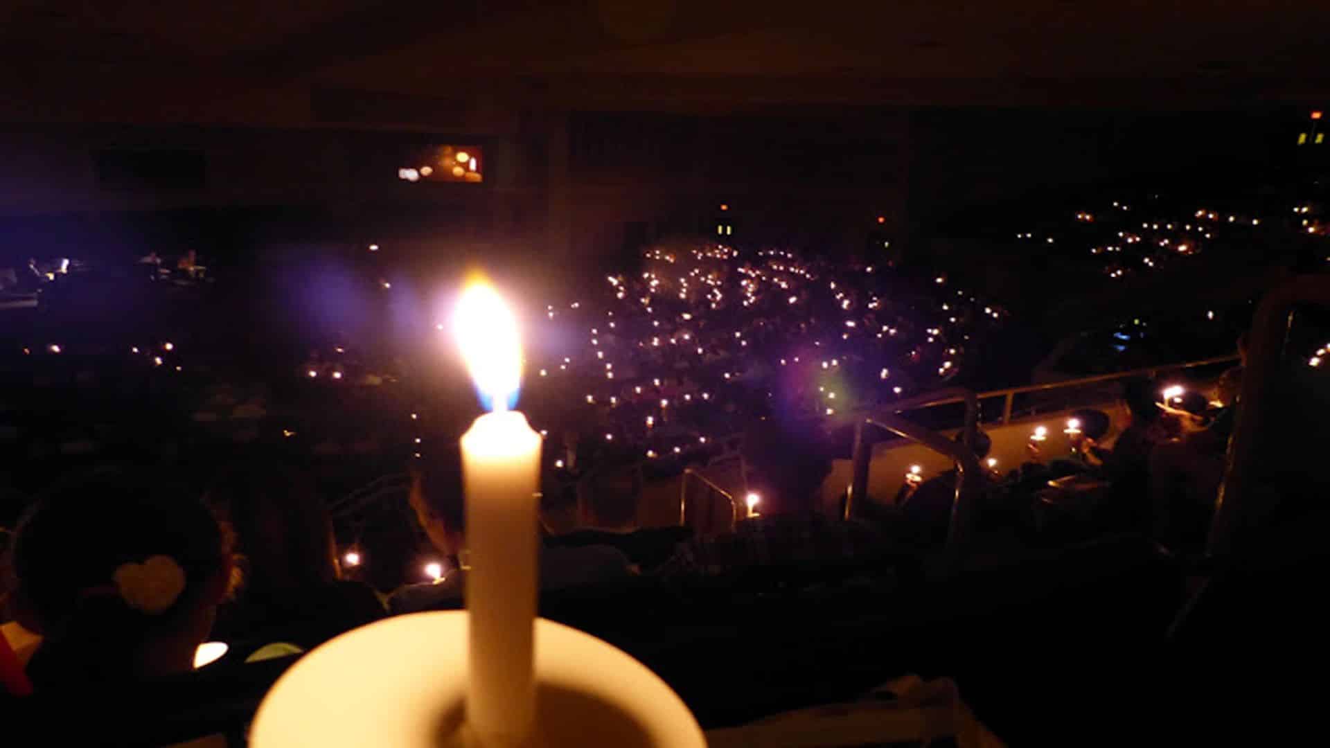 Close up of a lit candle with many other lit candles in the background